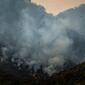 a helicopter is dwarved by a cloud of smoke from wildfires on a mountainside