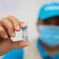 hand holding vaccine vial with blurred, masked face of health worker in background