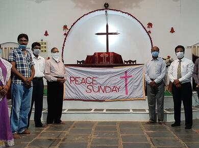 masked congregation members stand on either side of "Peace Sunday" banner draped altar