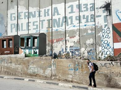 a man walks past a tall, graffitied concrete wall
