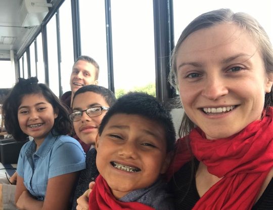 Two adults and three children smile while sitting next to each other