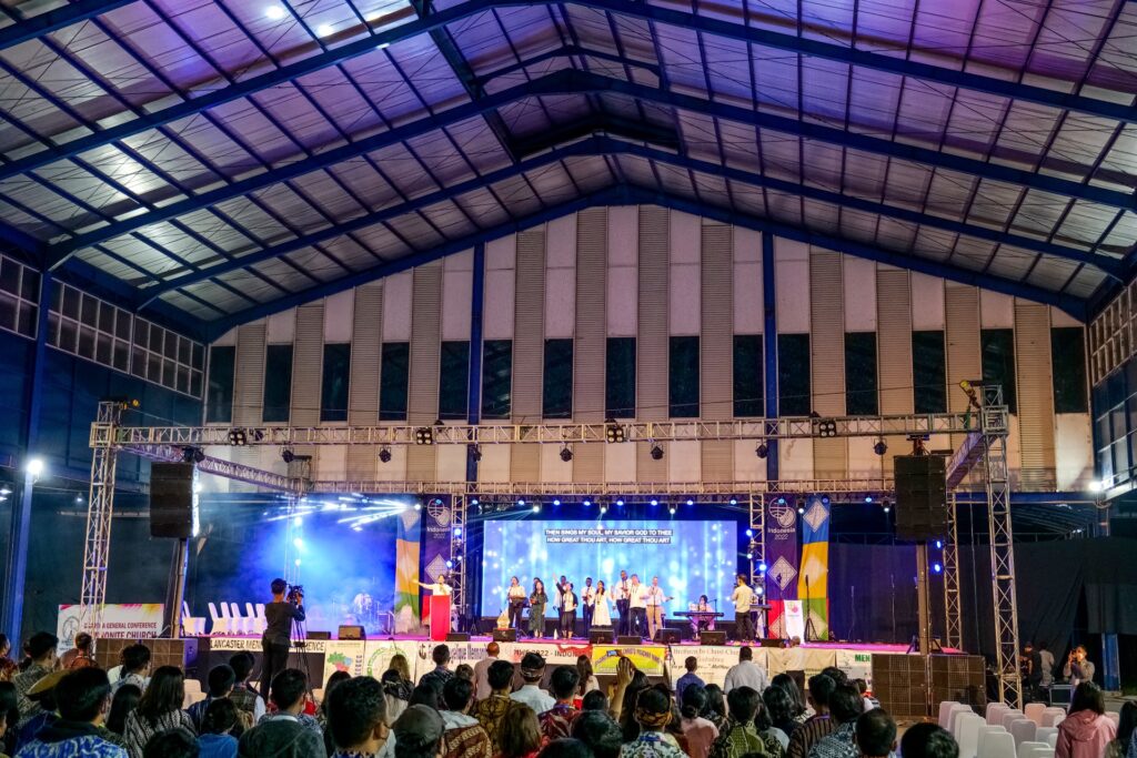 A Church service with people singing on stage and the crowd raising their hands