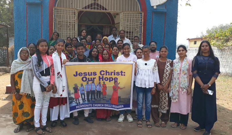 A group of people smile and hold us a sign that says "Jesus Christ: Our Hope"