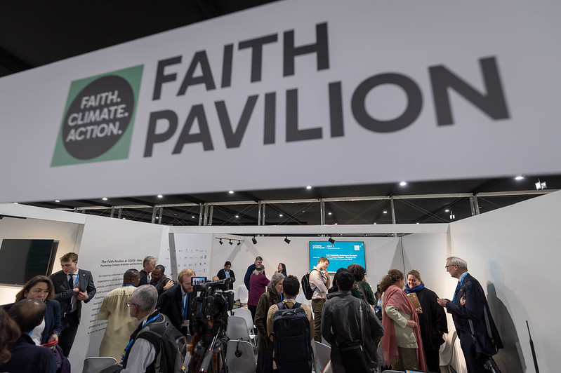 People mill about below a banner declaring Faith. Climate. Action. Faith Pavilion.