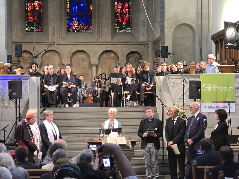 a woman behind a pulpit flanked by men in religious garb in a historic minster.