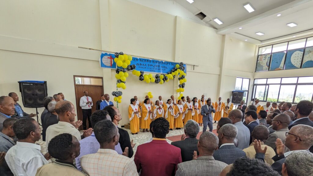 orange cloaked choir in front of room full of african spectators
