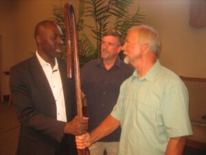 Calvin Greiner, an intercessor, presents a shepherd’s staff to Nemi Chigoji, ARC chair, representing the broader Mennonite Church. Lancaster Mennonite Conference Bishop Lloyd Hoover looks on.