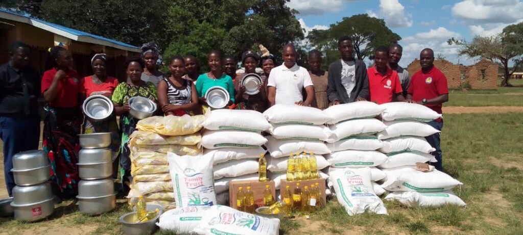 stack of rice bags and other food supplies with relief workers standing behind.