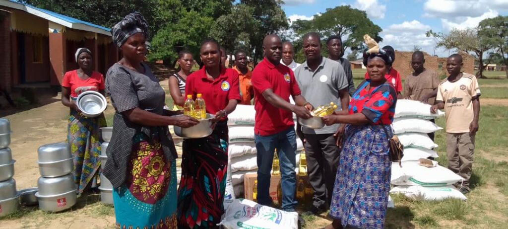 stack of rice bags and other food supplies with relief workers standing behind.