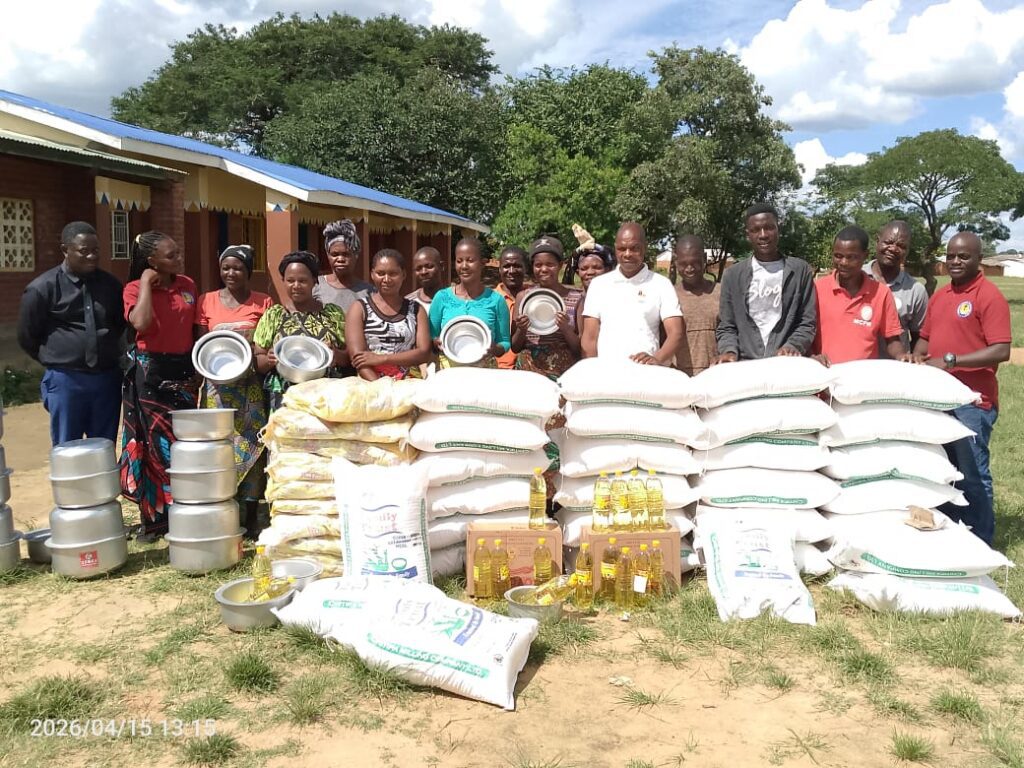 stack of rice bags and other food supplies with relief workers standing behind.